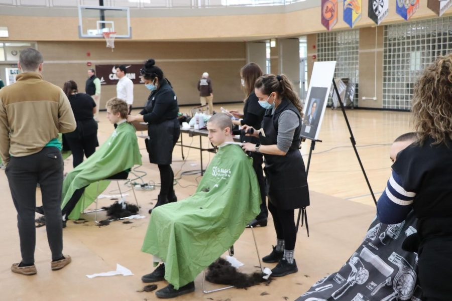 Sophomore Aiden Mattiello (seated left) and junior Simon Wheeler get their heads shaved at the 2022 St. Baldricks event on March 17. 