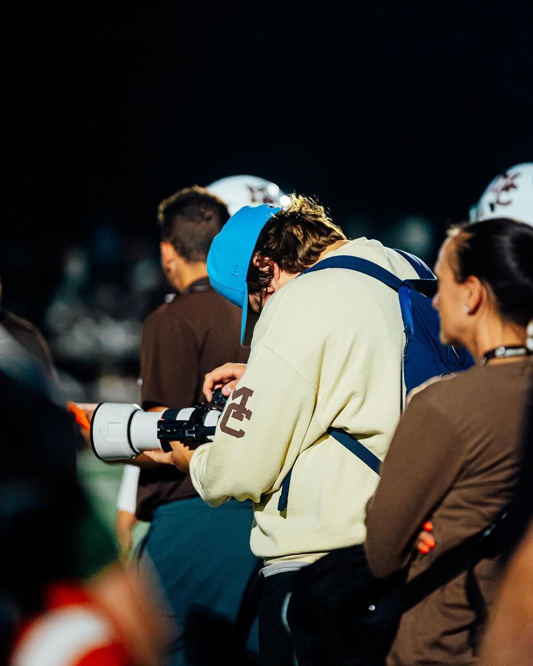 Rocco Lopez, the MC student behind shotsbyrocco, looks down at his camera to inspect a photo he just took at a Caravan football game. 